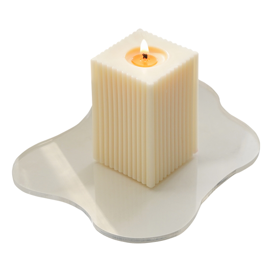 a lit ribbed rectangular soy pillar candle on irregular shape wavy acrylic coaster