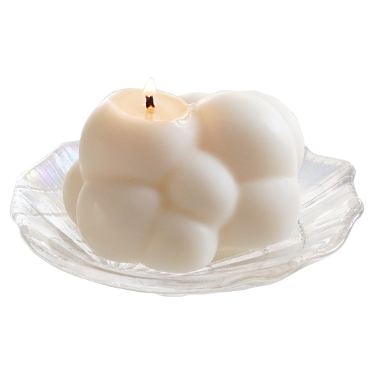 a lit cloud soy pillar candle on a holographic shell tray