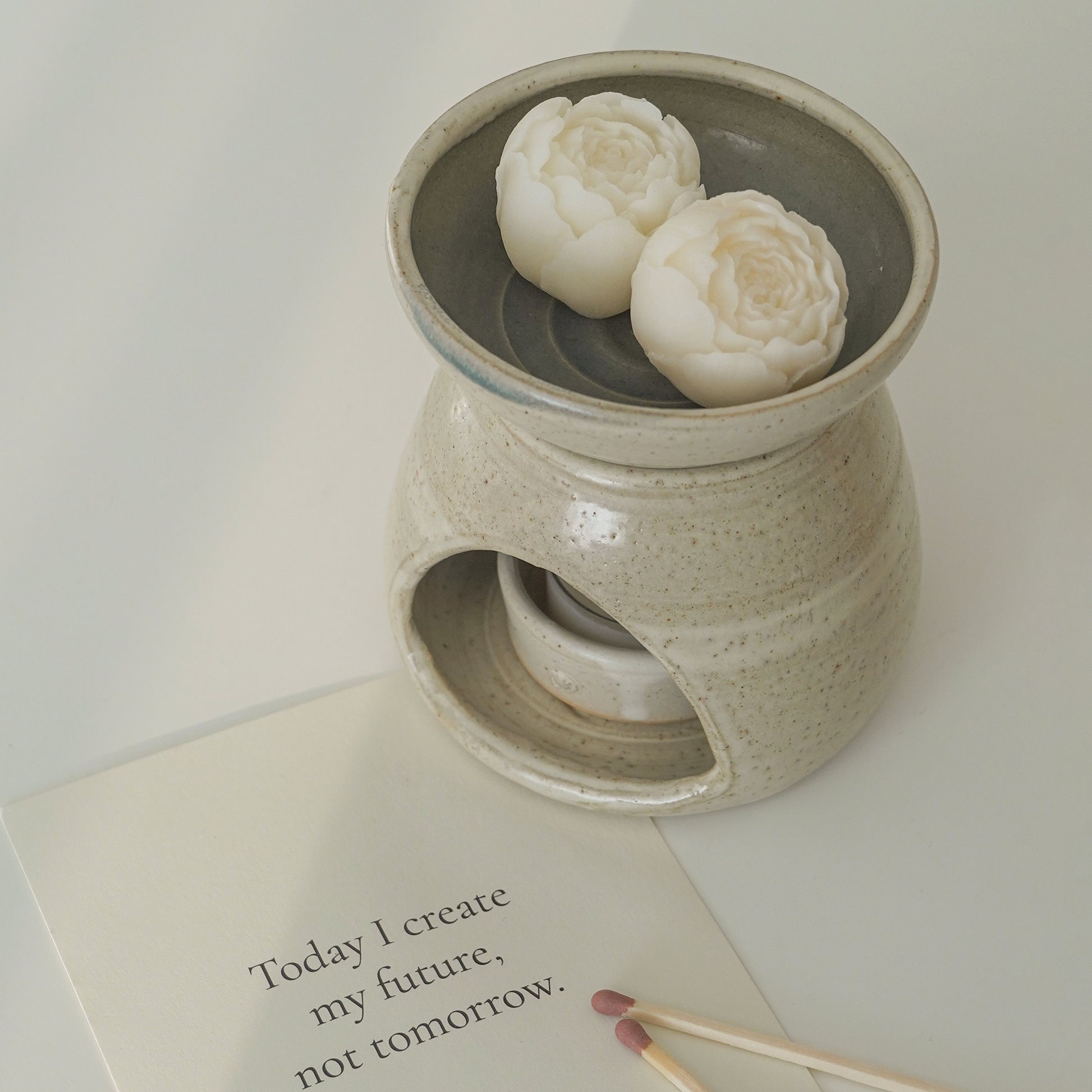 peony flower wax melts in a wax warmer, a white postcard inscribed with "Today I create my future, not tomorrow.", and brown matches