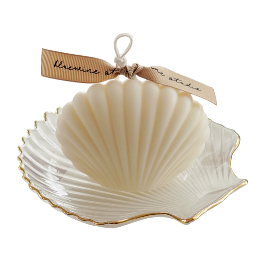 white seashell soy pillar candle with beige bluewine studio ribbon on a gold rim clear shell tray