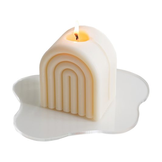 a lit white rainbow soy pillar candle on a clear wavy acrylic coaster