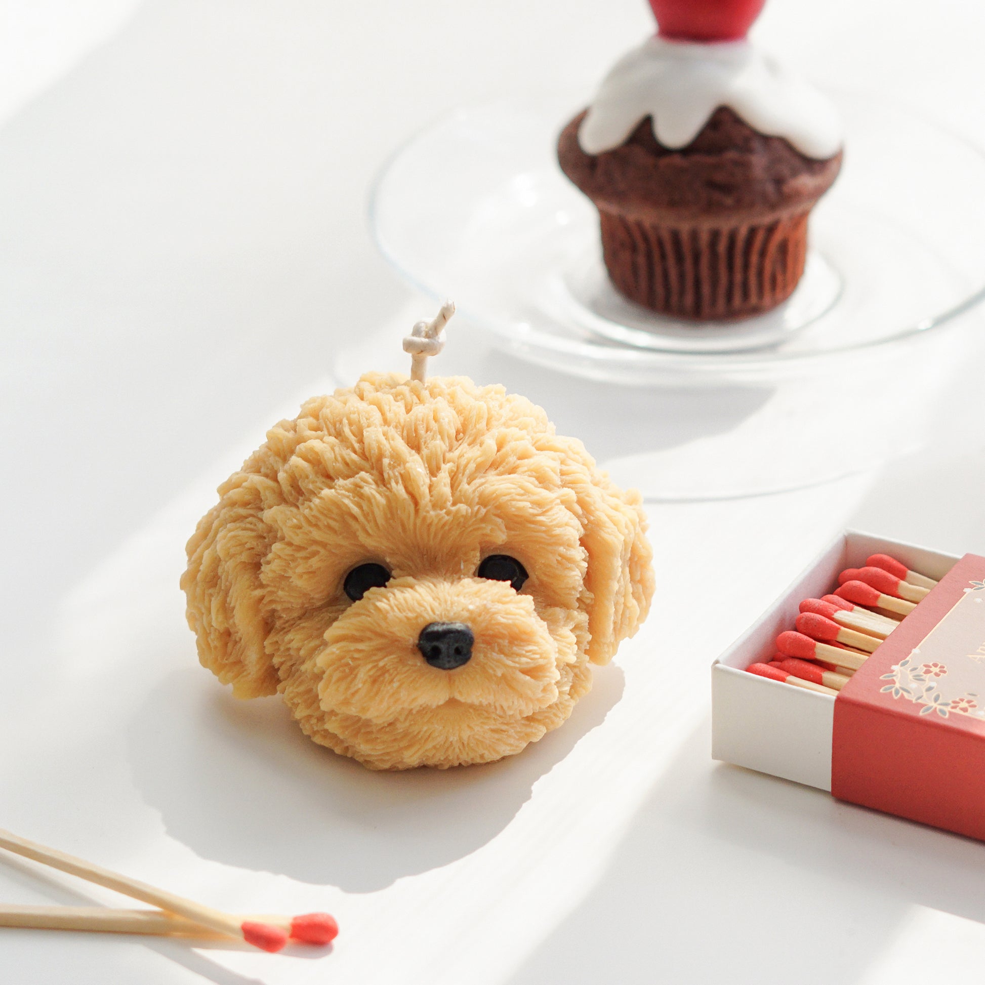 goldendoodle soy pillar candle, cherry muffin candle, chocolate cherry muffin candle on a glass plate, and matches on white table