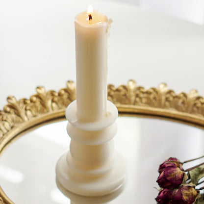 a lit white candlestick shape soy pillar candle and red rose dried flowers on round gold french mirror tray