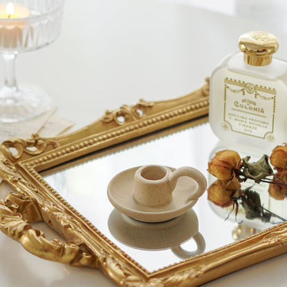dotted beige ceramic taper candle holder, yellow rose dried flowers, and santa maria novella perfume placed on rectangular gold french mirror tray on white table
