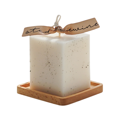 a dotted white square pillar candle with beige bluewine studio ribbon on a square wood coaste