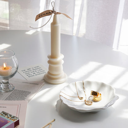 candlestick shape white soy pillar candle with beige bluewine studio ribbon, a lit tealight candle in a mini glass, mint color matches, newspapers, a postcard, French book called Beau Jeu, gold earrings and necklace on white ceramic shell tray on white round table