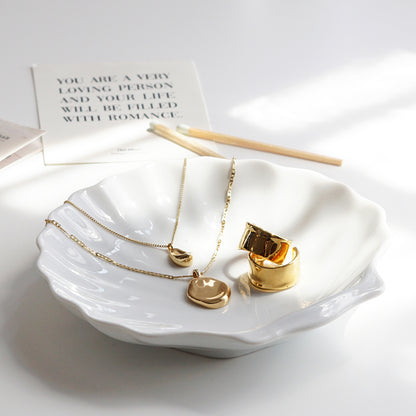 Jenny Bird necklace and earrings on white ceramic shell tray, a postcard and matches on white table