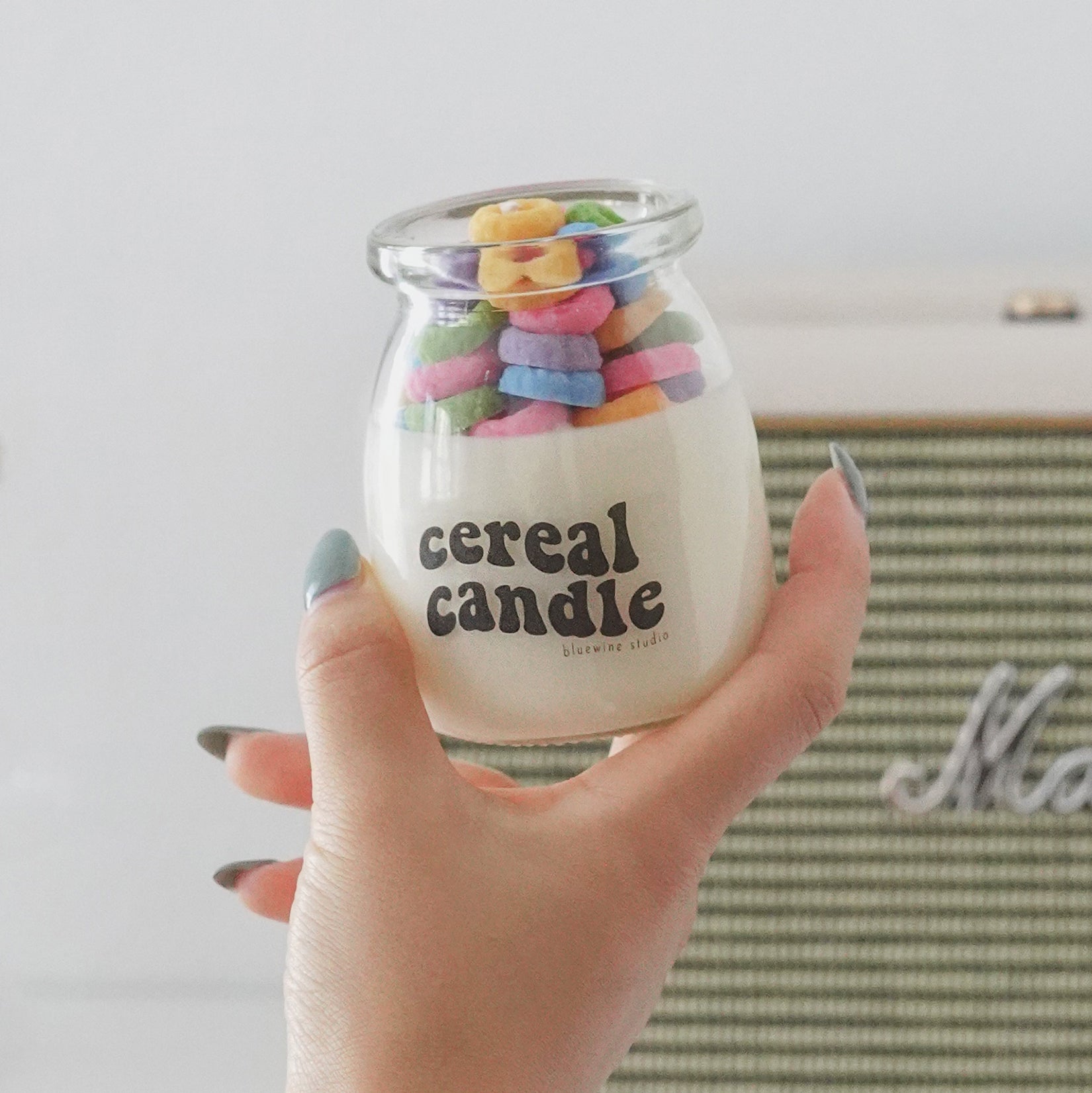 a hand holding a colorful fruit loops cereal candle with marshall speaker and yellow dried flowers in a vase in the back