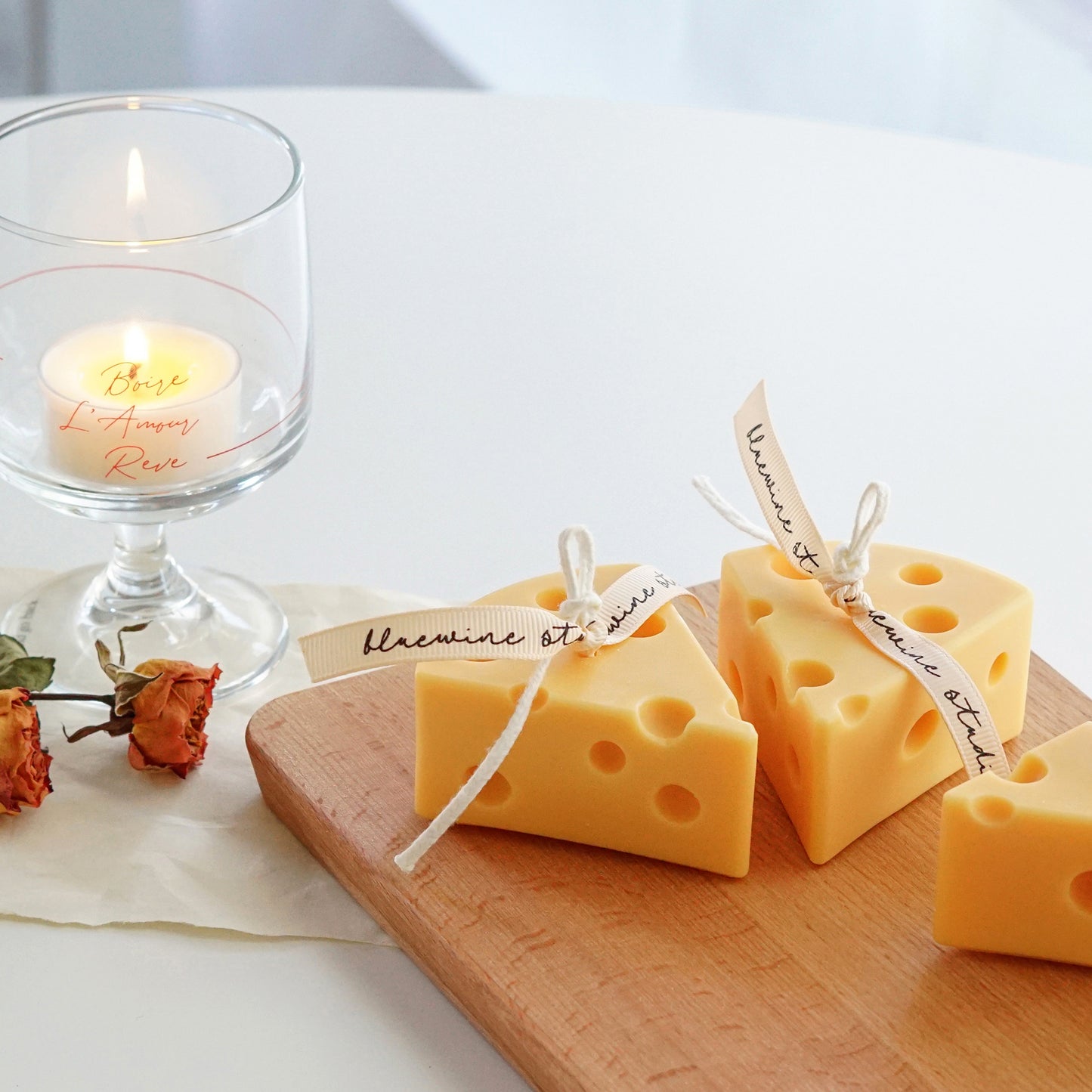 cheese soy pillar candles on wood board, dried flowers, and a lit tealight candle in a mini glass on white round table