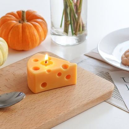 a lit slice of cheese soy pillar candle on a mini wood board