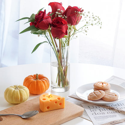 a lit cheese soy pillar candle on wood board, cookie candles on white plate, mini pumpkins, and roses in a clear vase on white round table