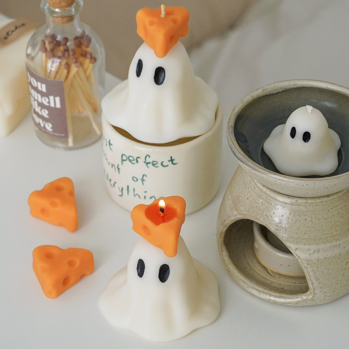 ghost candles with cheese on top, cheese wax melts, wax warmer, mug, and match bottle on a vanity table