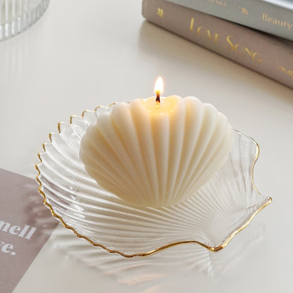 a lit white seashell soy pillar candle on a gold rim clear shell tray, two books, you smell like love beige postcard