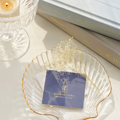 navy blue color bluewine studio business card and dried gypsophila placed on gold rim clear shell tray, a lit tealight candle in a glass coupe, and two books stacked together