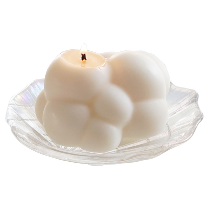 a lit cloud soy pillar candle on a holographic shell tray