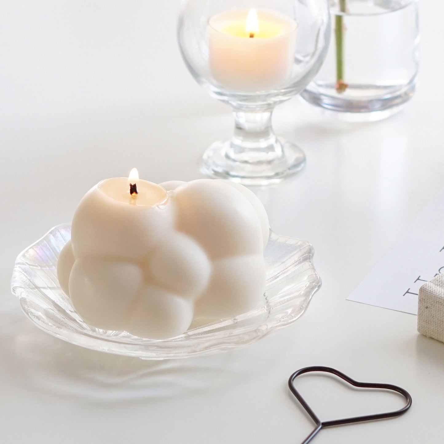 a lit minimal dreamy aesthetic cute white cloud soy pillar candle on a holographic shell tray