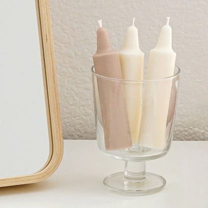 ikea vanity mirror, a beige crayon candlee, two white soy pillar cloud candles in a glass