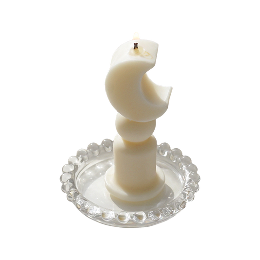 a lit dreamy aesthetic crescent moon shaped soy pillar candle on a clear beaded round tray