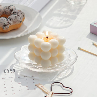 a lit white square cube bubble soy pillar candle on a holographic shell tray, september calendar postcard, heart wick dipper, mint color matches, and oreo cookie mochi donut on a white ceramic plate