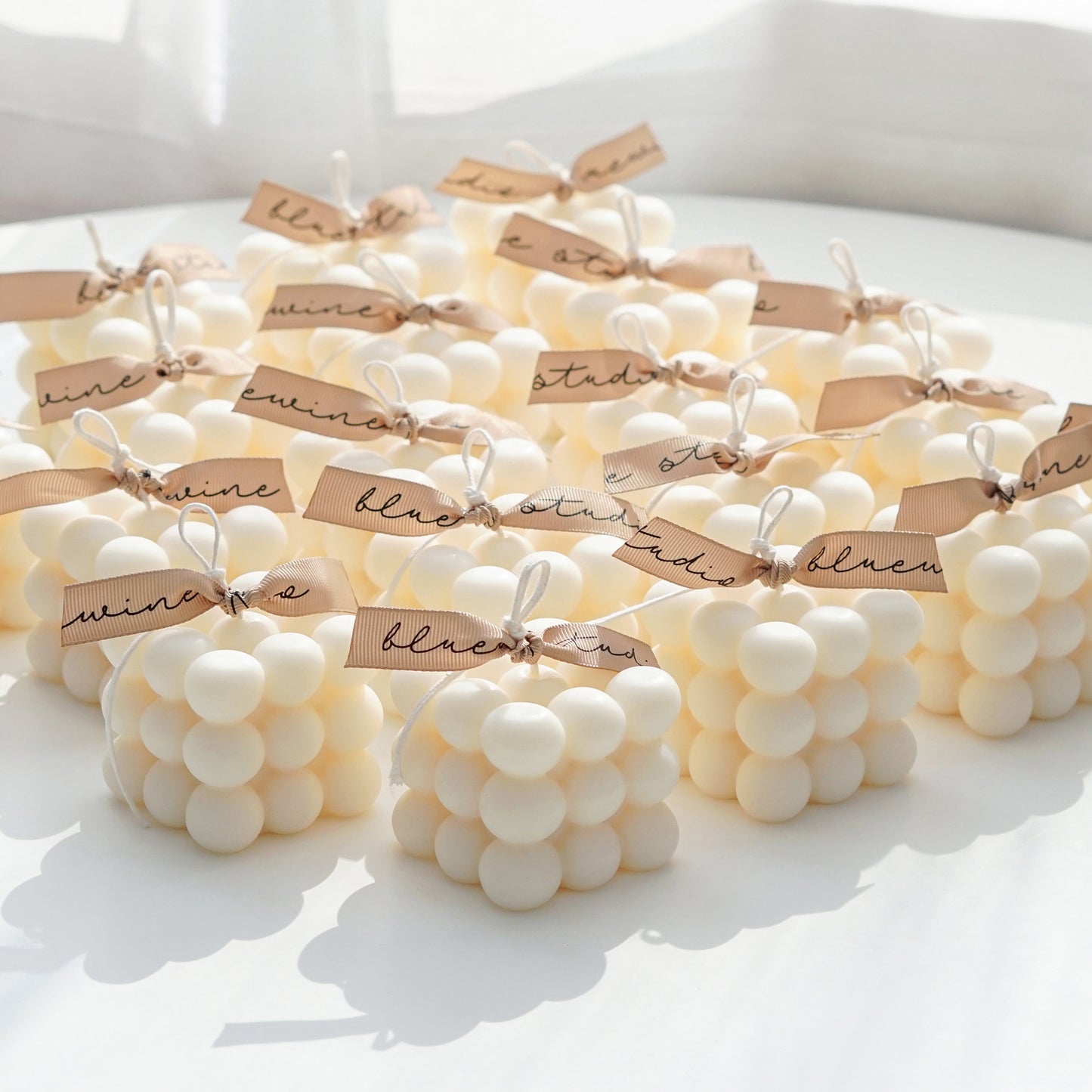 twenty white cube bubble square soy pillar candle with beige bluewine studio ribbon are placed on white round table for party favors