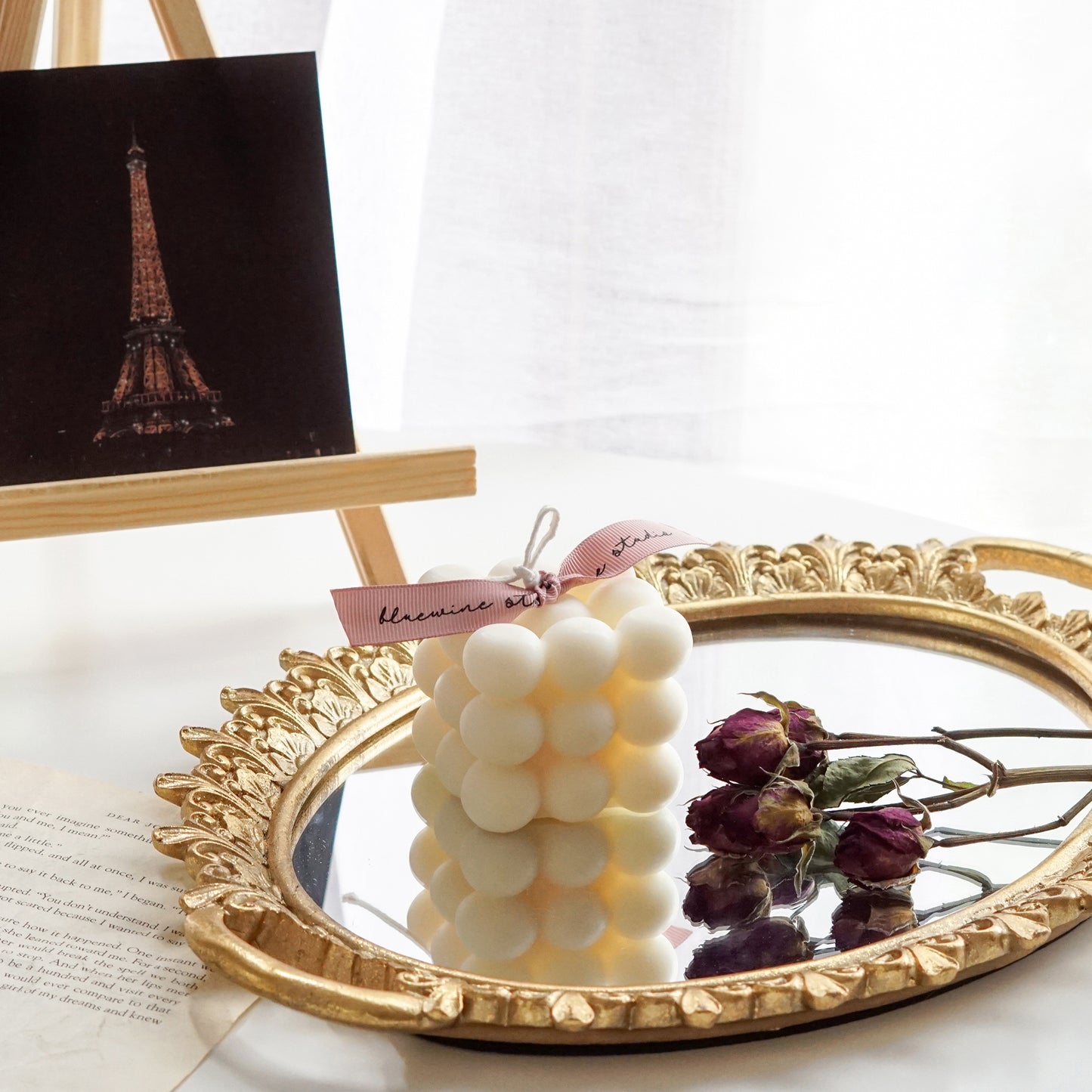 a cube shape bubble soy pillar candle and dried burgundy roses on french style oval shape gold mirror tray