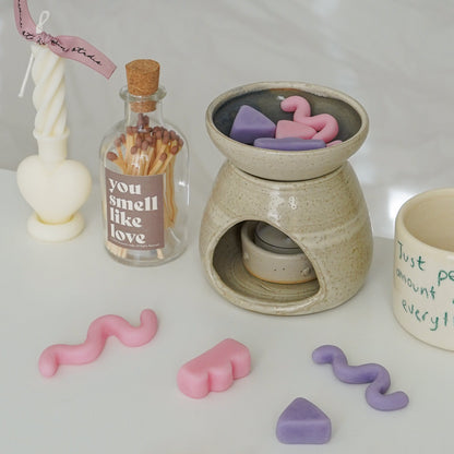 pastel geometric shape unique wax melts in a wax warmer, a match bottle, a heart twist candle, and a mug on white table