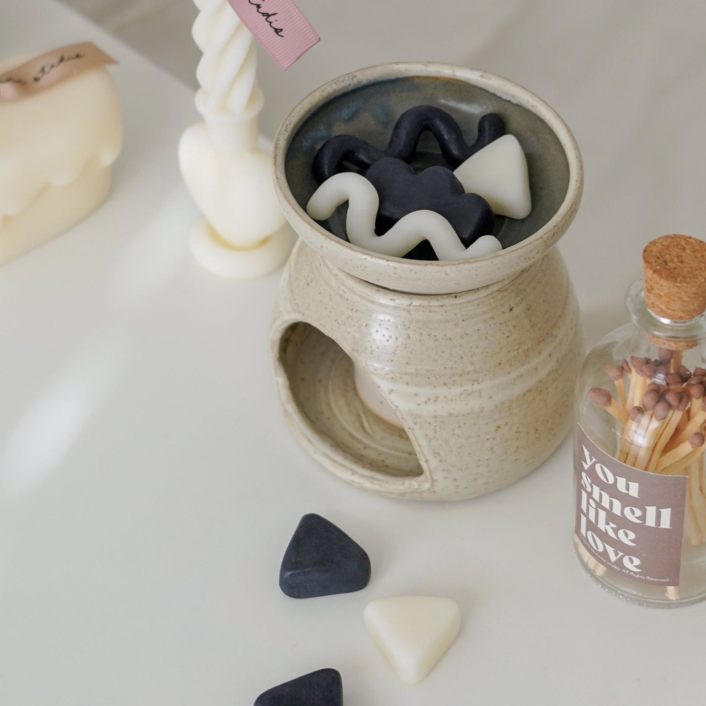 black and white geometric shape unique wax melts in a wax warmer, a match bottle, and a heart twist candle on white table