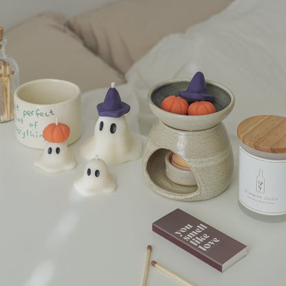 purple wizard hat ghost candle, mini ghost candles, frosted glass container soy candle with wooden lid, halloween wax melts in a wax warmer, and a brown matchbox inscribed with you smell like love on white table in a cozy room