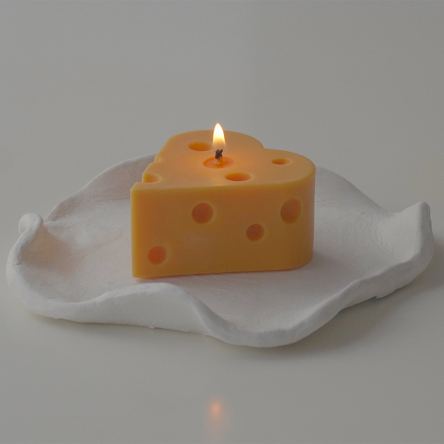 a lit heart cheese candle on a white irregular clay tray