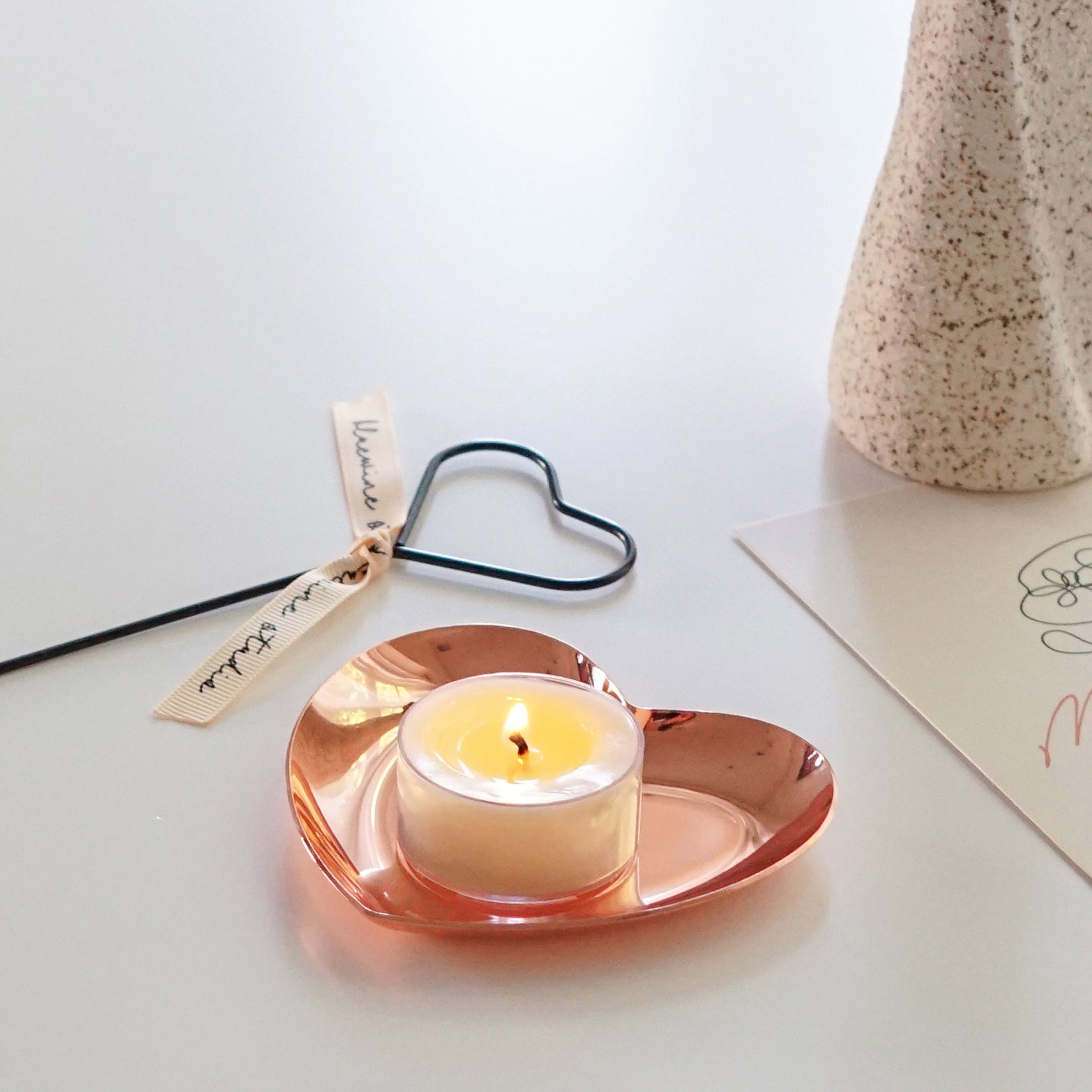 a lit tealight candle on rose gold heart shape tray with heart candle wick dipper