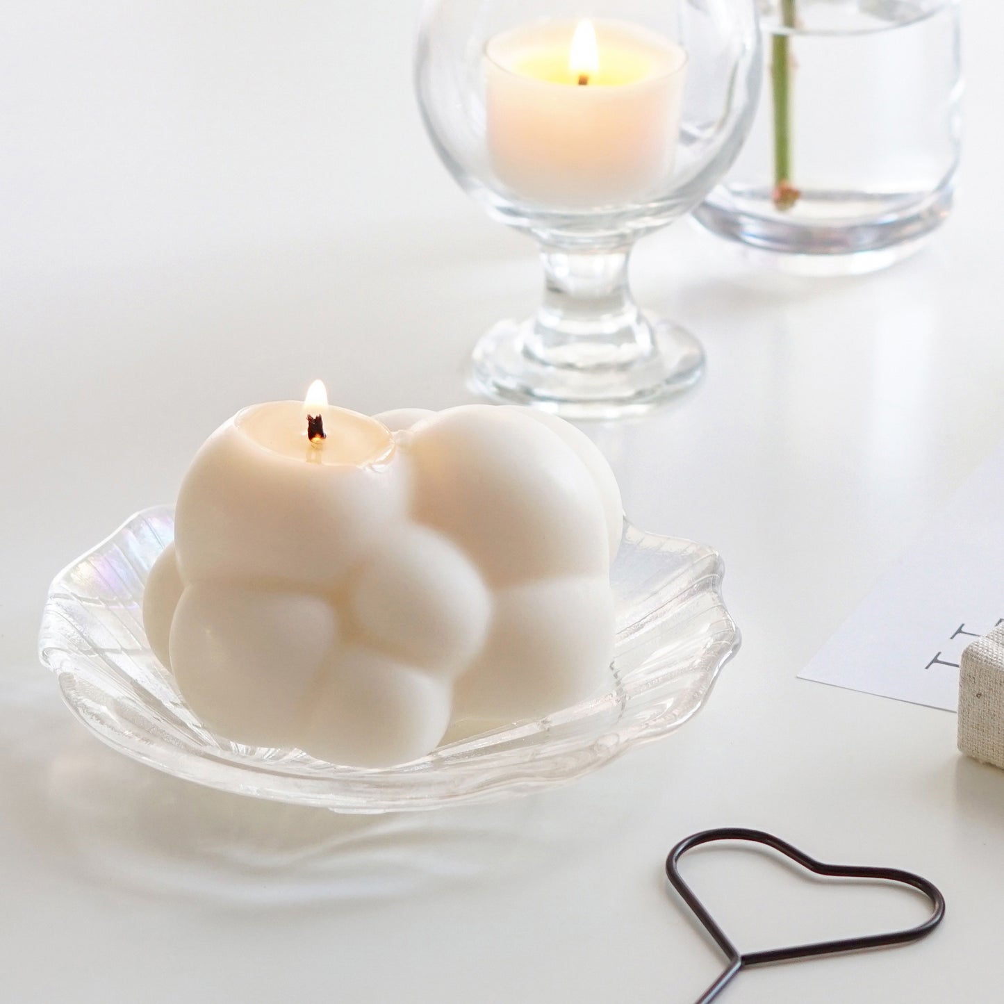a lit white cloud soy pillar candle on a holographic shell tray