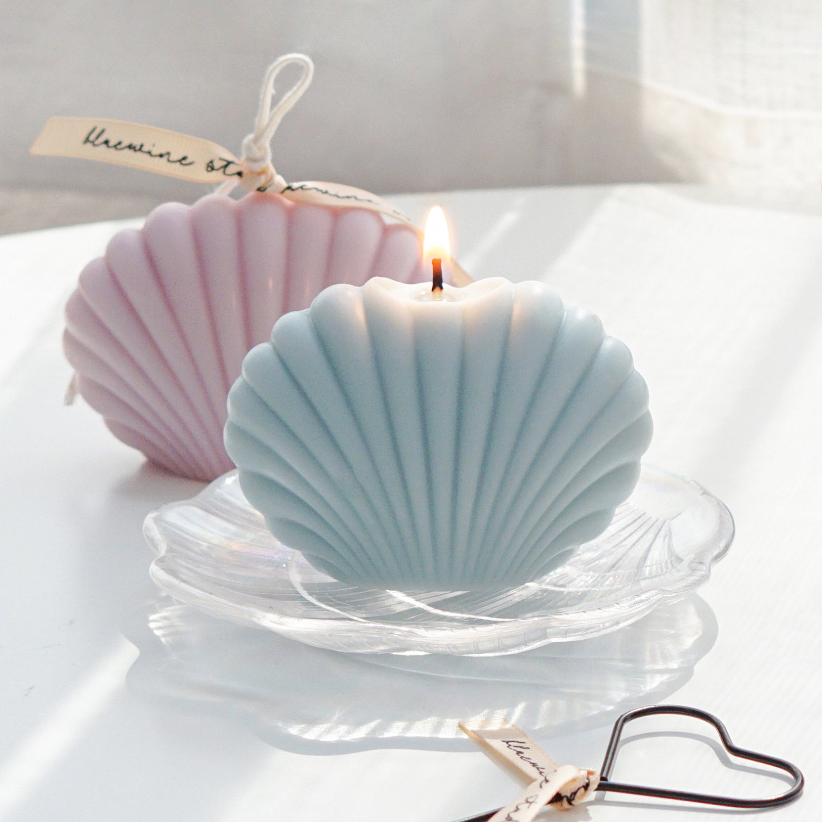 a lit aqua blue color seashell soy pillar candle on a holographic shell tray and lavender shell candle