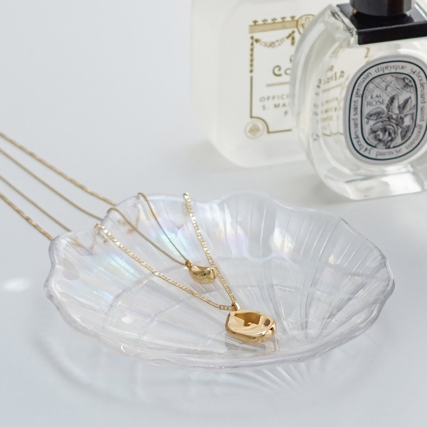 jenny bird gold round necklace on a holographic shell tray, diptyque rose perfume, and santa maria novella perfume