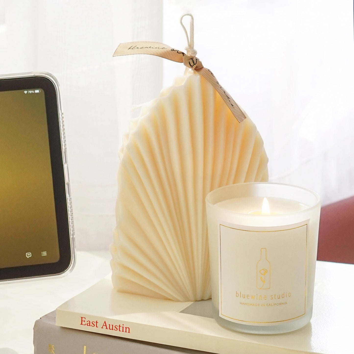 a leaf shape sculptural white natural soy pillar candle and a lit 5oz frosted glass container candle on book stacks and ipad mini playing music messages from her by sabrina claudio