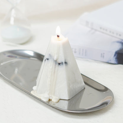 a lit pentagonal pyramid shape marble candle on a silver oval tray