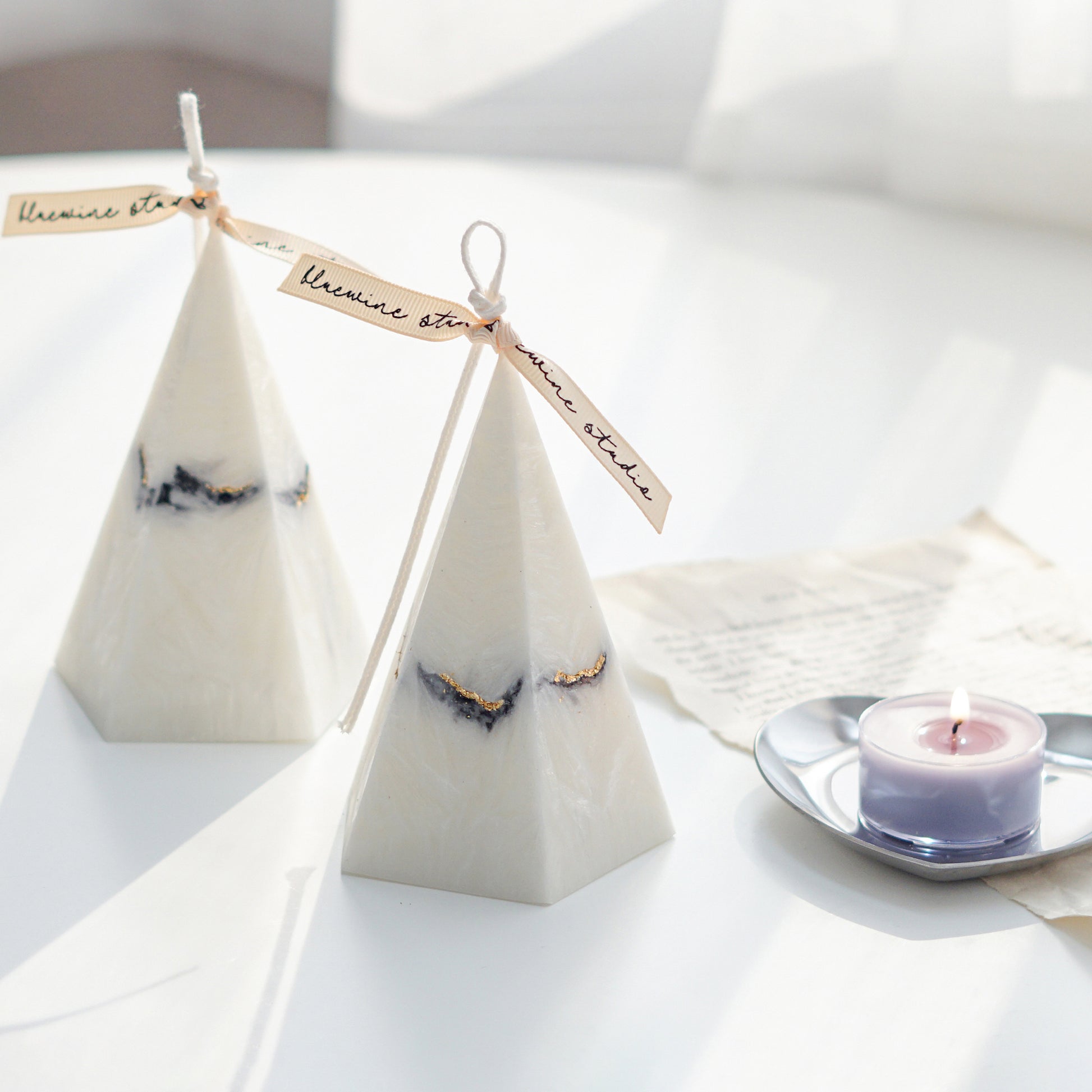 two pentagonal pyramid shape marble candles with gold glitters and lavender color lit tealight candle on a silver heart shape tray