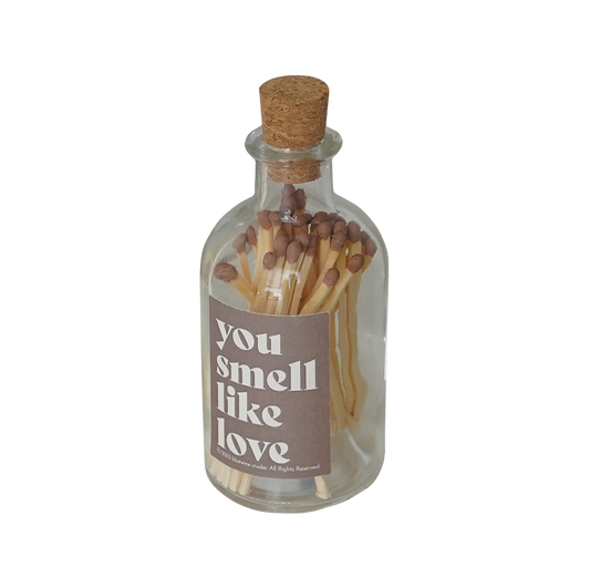 a glass match bottle filled with brown matches and a brown sticker inscribed with "you smell like love"