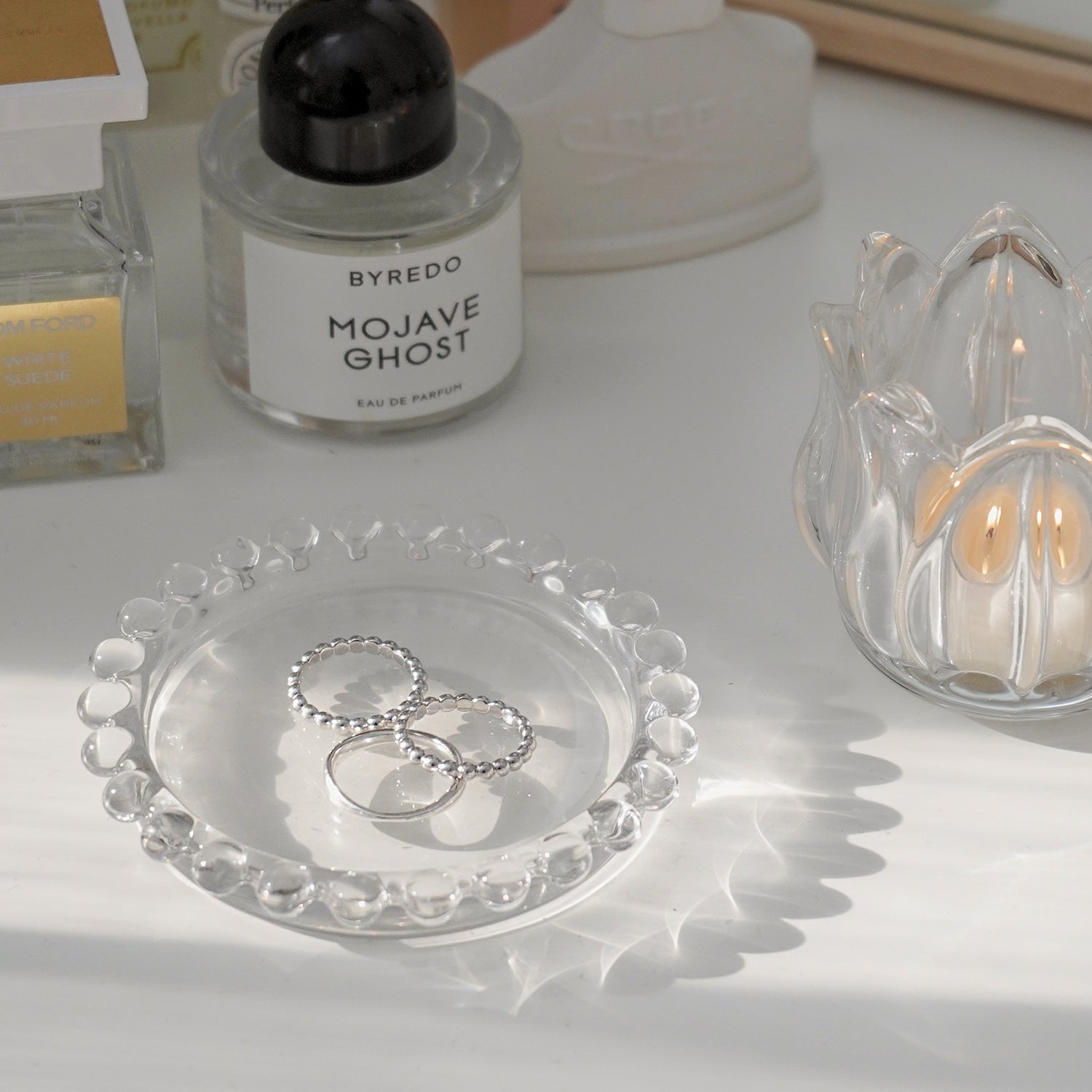 mini beaded clear round tray with silver rings and a lit tealight candle in a tulip flower shape glass tealight candle holders on vanity table with byredo, creed, and tom ford perfumes
