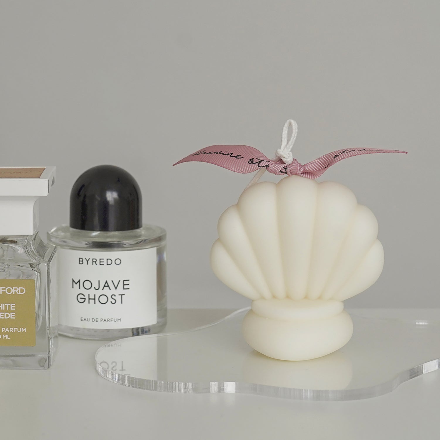 shell shaped soy pillar candle on a clear irregular shape acrylic coaster and perfumes on vanity table