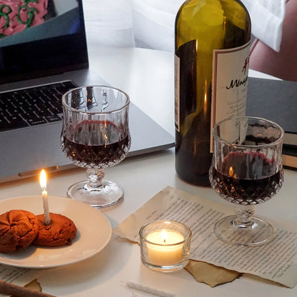 red wine in a mini wine glass, cookies on ceramic white dish, mini cake candles in a glass, a lit tealight candle in a glass candle holder, a bottle of wine, book pages, and macbook displaying a movie scene from harry potter