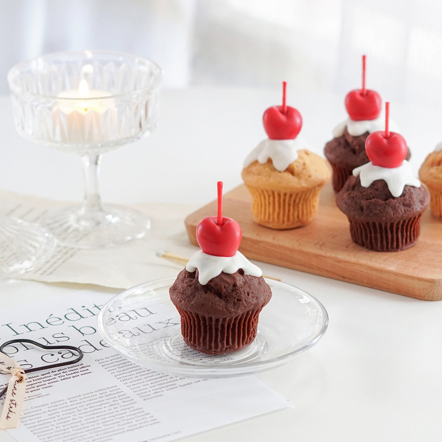 chocolate muffin with cherry on top soy pillar candle on clear dish and muffin candles on mini wood board in the back