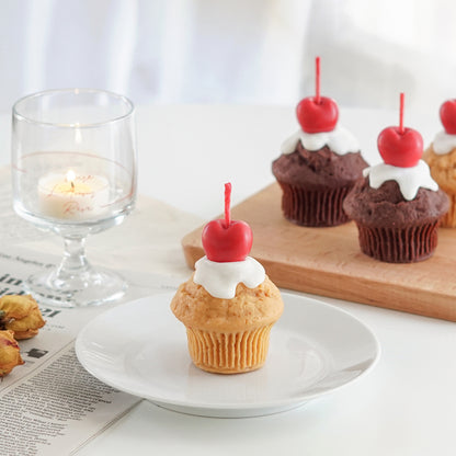 vanilla muffin with cherry on top soy pillar candle on clear dish and muffin candles on mini wood board in the back