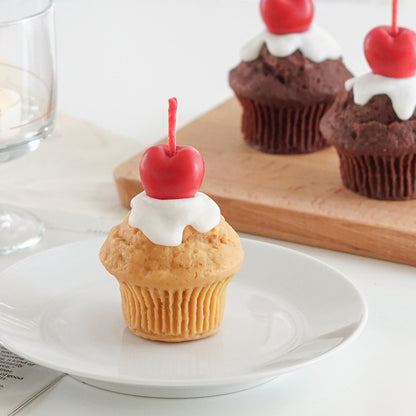 vanilla muffin with cherry on top soy pillar candle on clear dish and muffin candles on mini wood board in the back