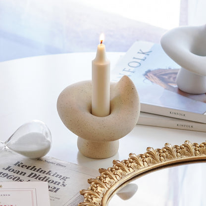 a lit white soy pillar crayon shape taper candle in a dotted beige mushroom shape candle holder, an hourglass, a round gold french mirror tray, and a white ceramic mushroom candle holder placed on Kinfolk magazines