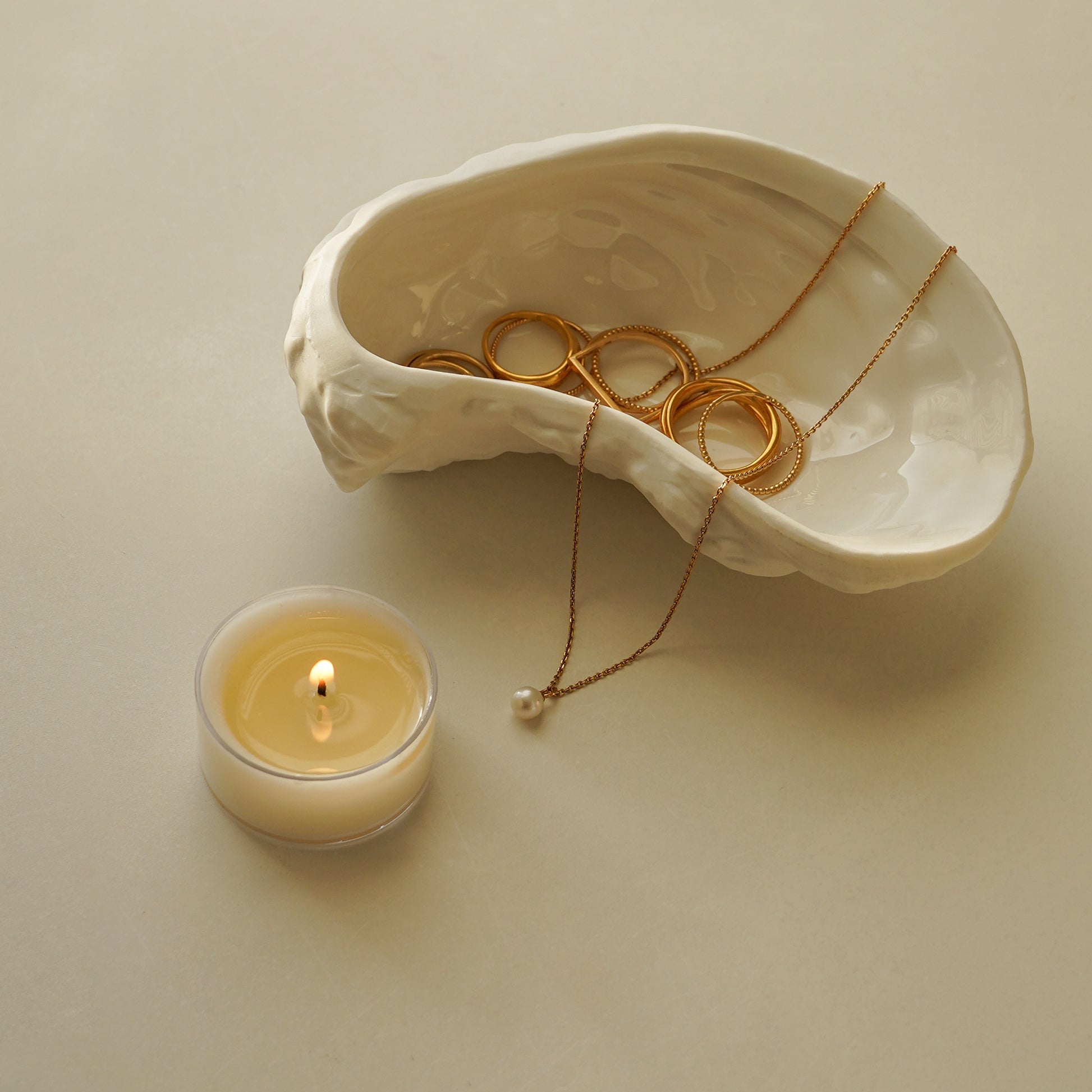 gold jewelry in oyster dish and a lit tealight candle