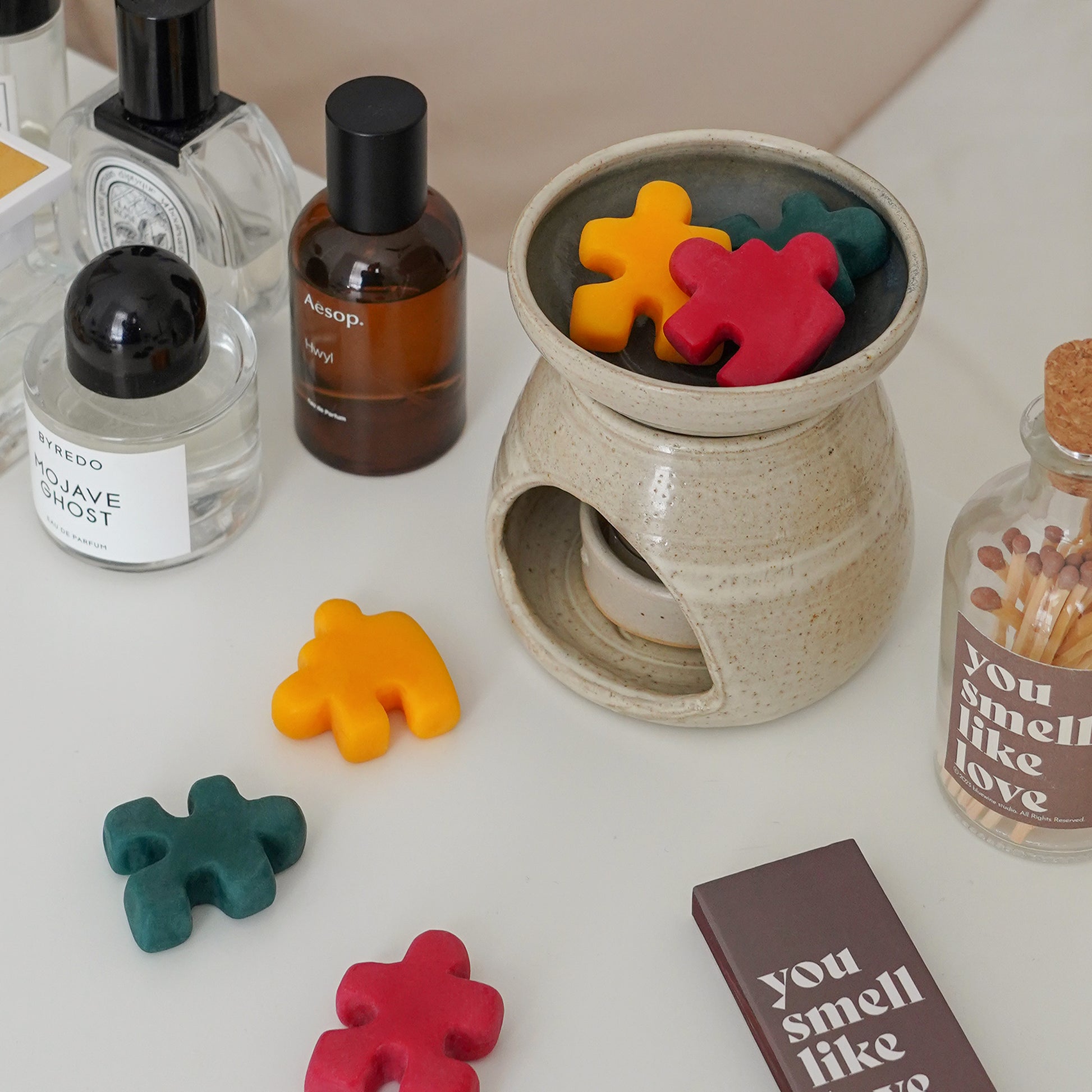 red, yellow, and green puzzle shape wax melts in a wax warmer, fragrances, a match bottle and a matchbox inscribed with "you smell like love"