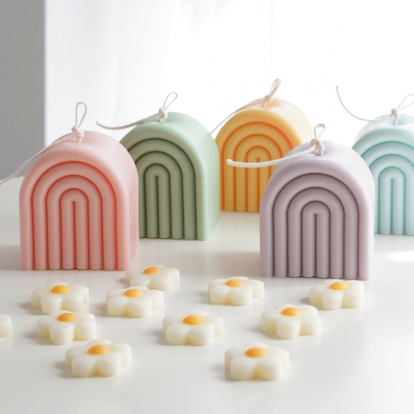 aqua blue, blush pink, lavender, sage green, and tangerine yellow rainbow shape arch pastel color soy pillar candles with long wicks and daisy wax melts on white round table