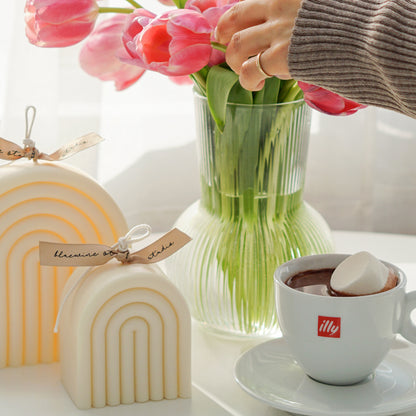 rainbow arch shaped white soy pillar candles, hot chocolate with marshmallow in illy mug set, and pink tulips in clear fluted vase on the white round table