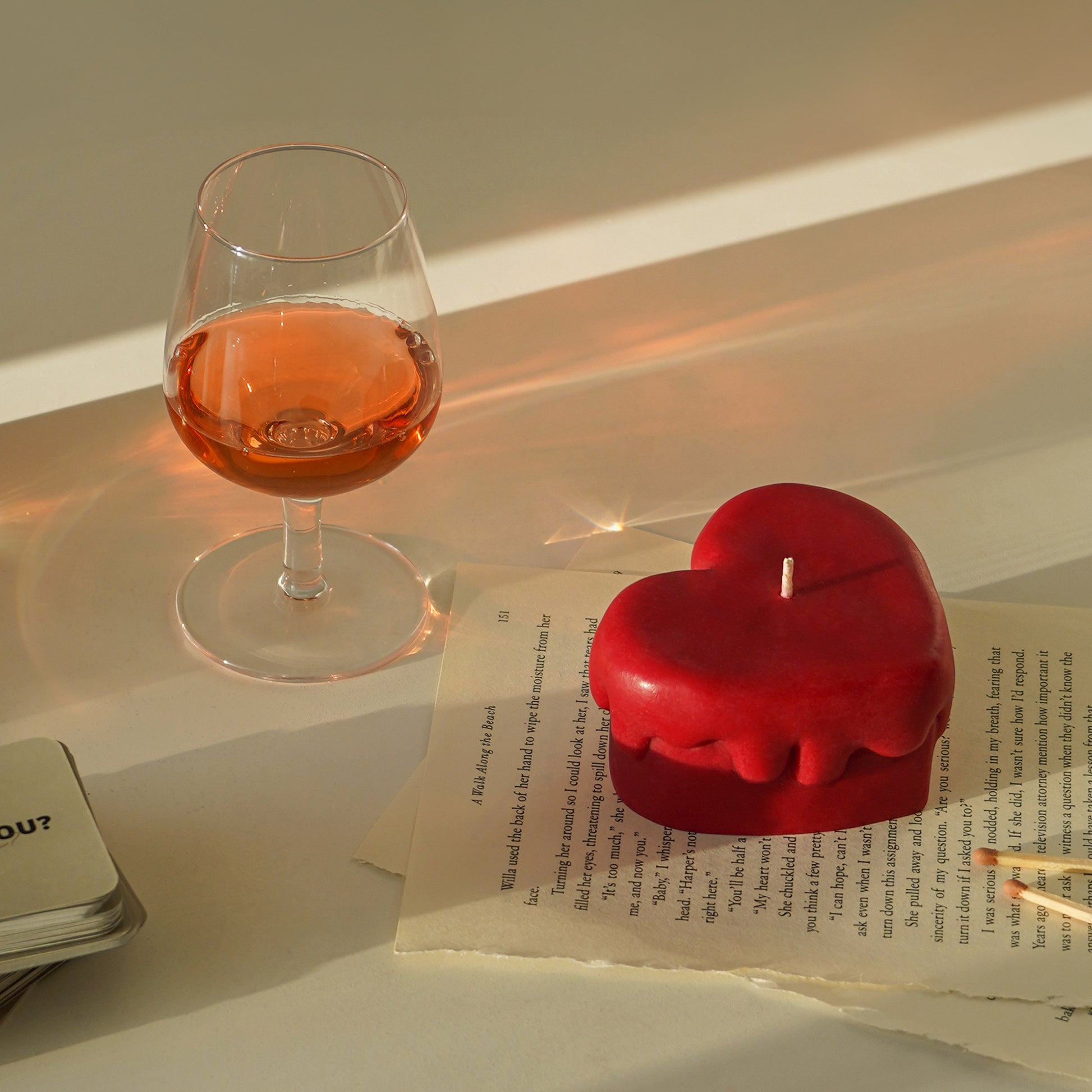 red melting heart candle on book pages and a glass of rose wine