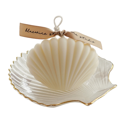 white seashell soy pillar candle with beige bluewine studio ribbon on a gold rim clear shell tray